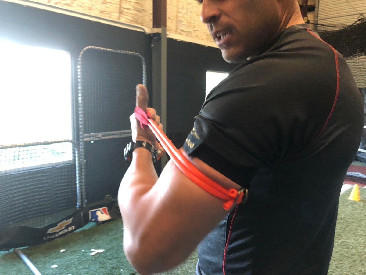 A coach in a batting cage wearing the Power Punch with orange tubing