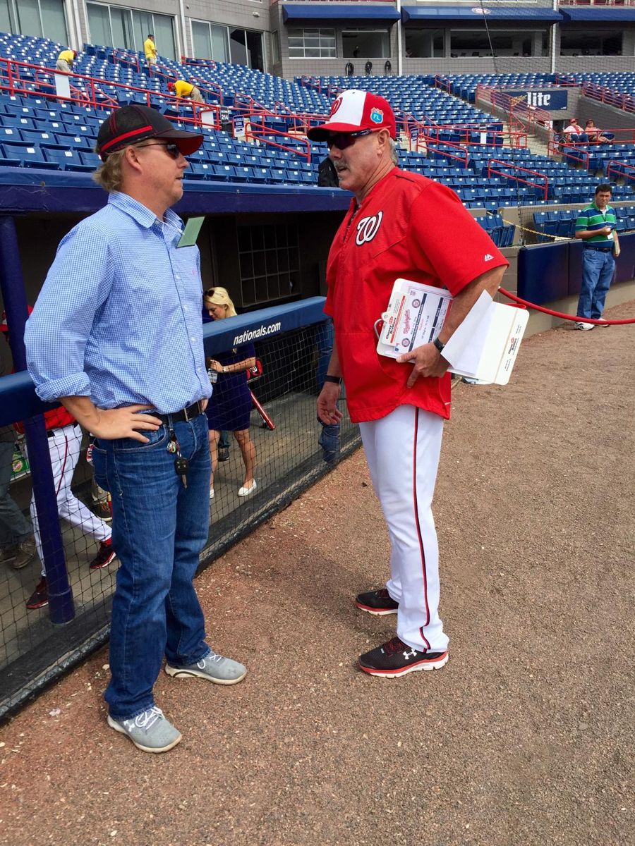 Kevan Burns talking with a coach beside a big-league spring training dugout