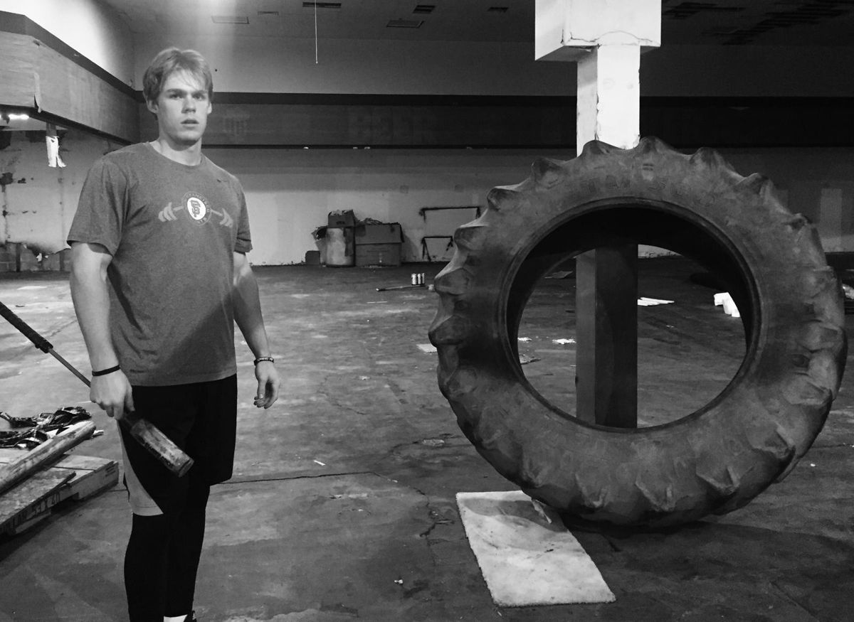 A young hitter holding a sledgehammer beside a tractor tire in an empty building